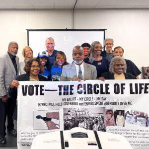 A group smiles in front of a projection screen holding a banner titled, Vote—The Circle of Life.