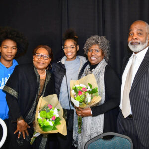Several people posing at a formal event. Two women are holding flowers.