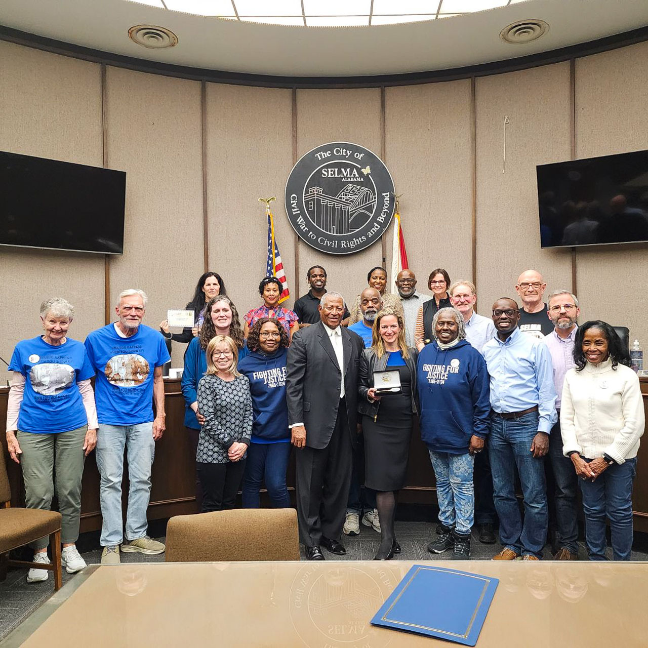 A large group smiles below a seal that reads, "The City of Selma, Alabama, Civil War to Civil Rights and Beyond."